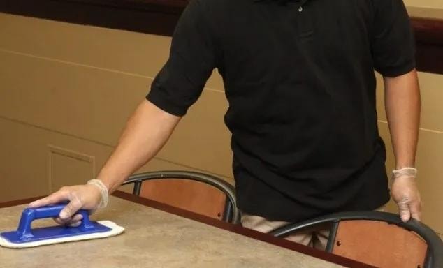 Facility worker cleaning a surface with a pad